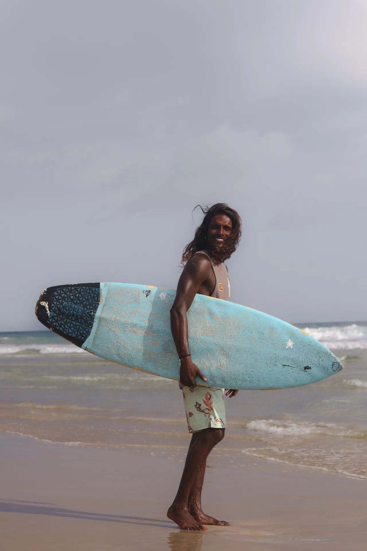 Home Waves surfer carrying a turquoise surfboard at Kabalana Beach